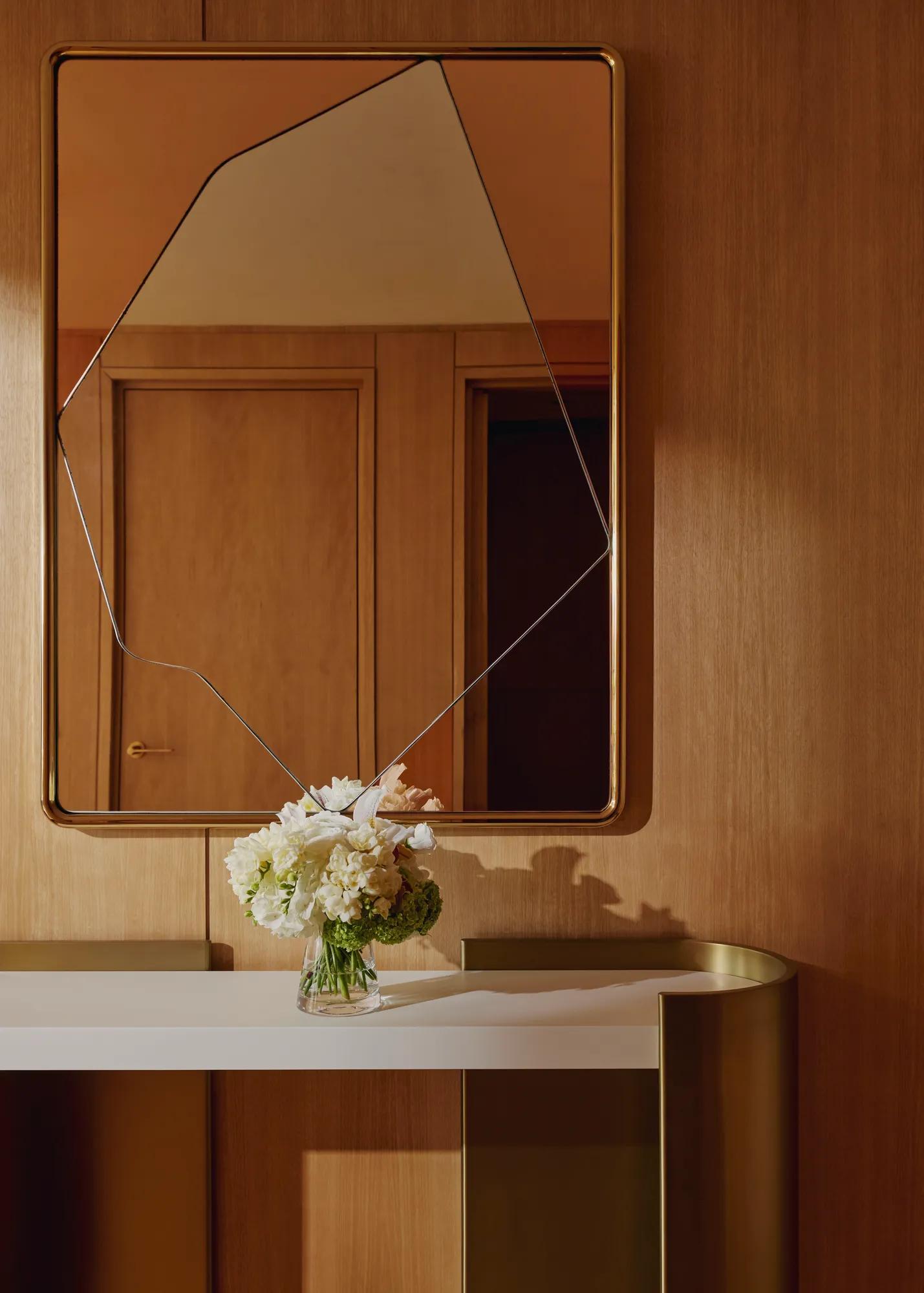 Minimalist white console table beneath an abstract mirror, decorated with a vase of fresh white flowers.