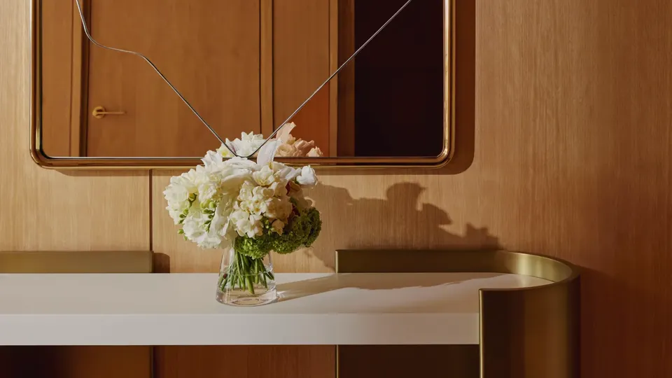 Minimalist white console table beneath an abstract mirror, decorated with a vase of fresh white flowers.