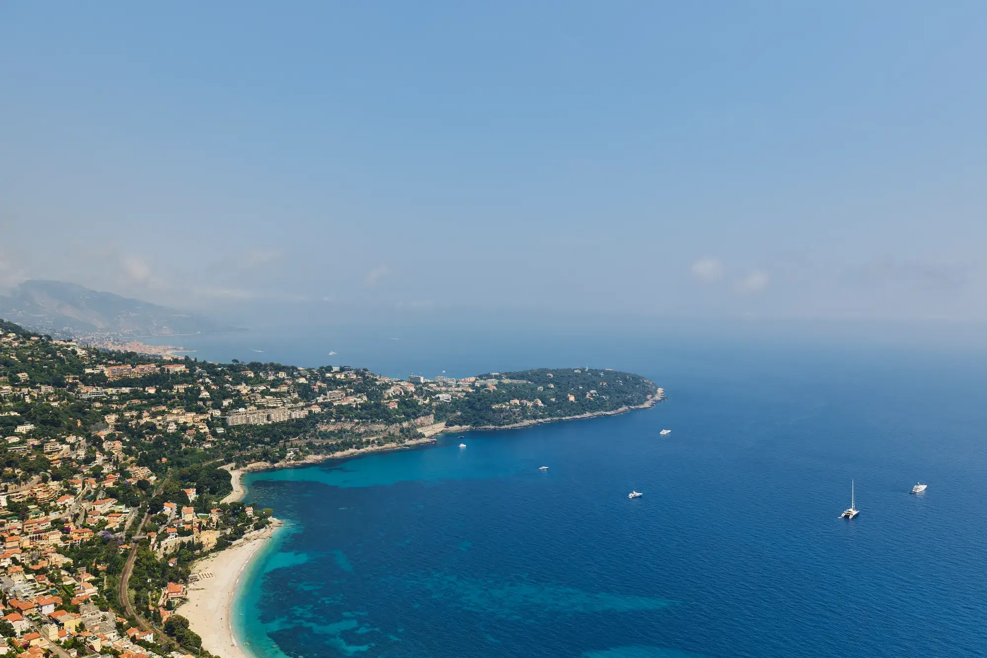 Aerial view of the French Riviera coastline with turquoise bays, hillside villas and boats on the Mediterranean Sea.