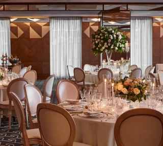 Ballroom with round tables, white chairs, and floral centrepieces lit by candles for an elegant wedding reception.