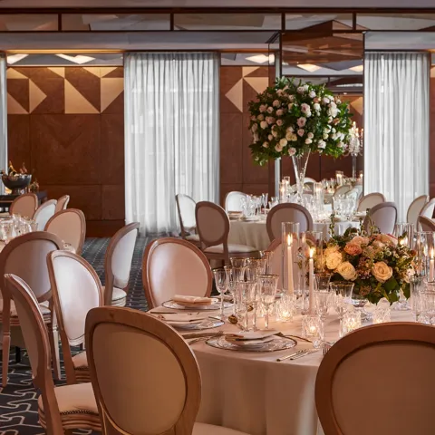Ballroom with round tables, white chairs, and floral centrepieces lit by candles for an elegant wedding reception.