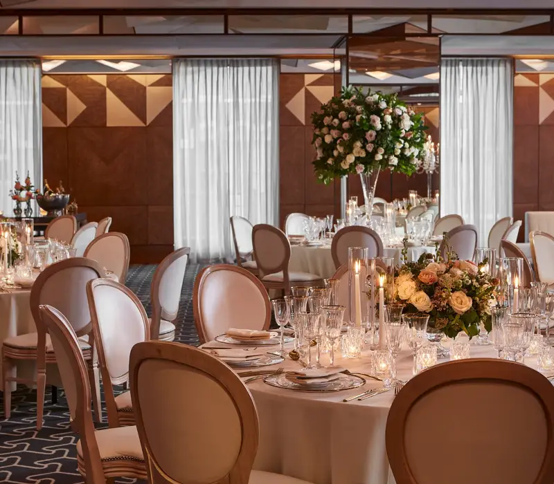 Ballroom with round tables, white chairs, and floral centrepieces lit by candles for an elegant wedding reception.