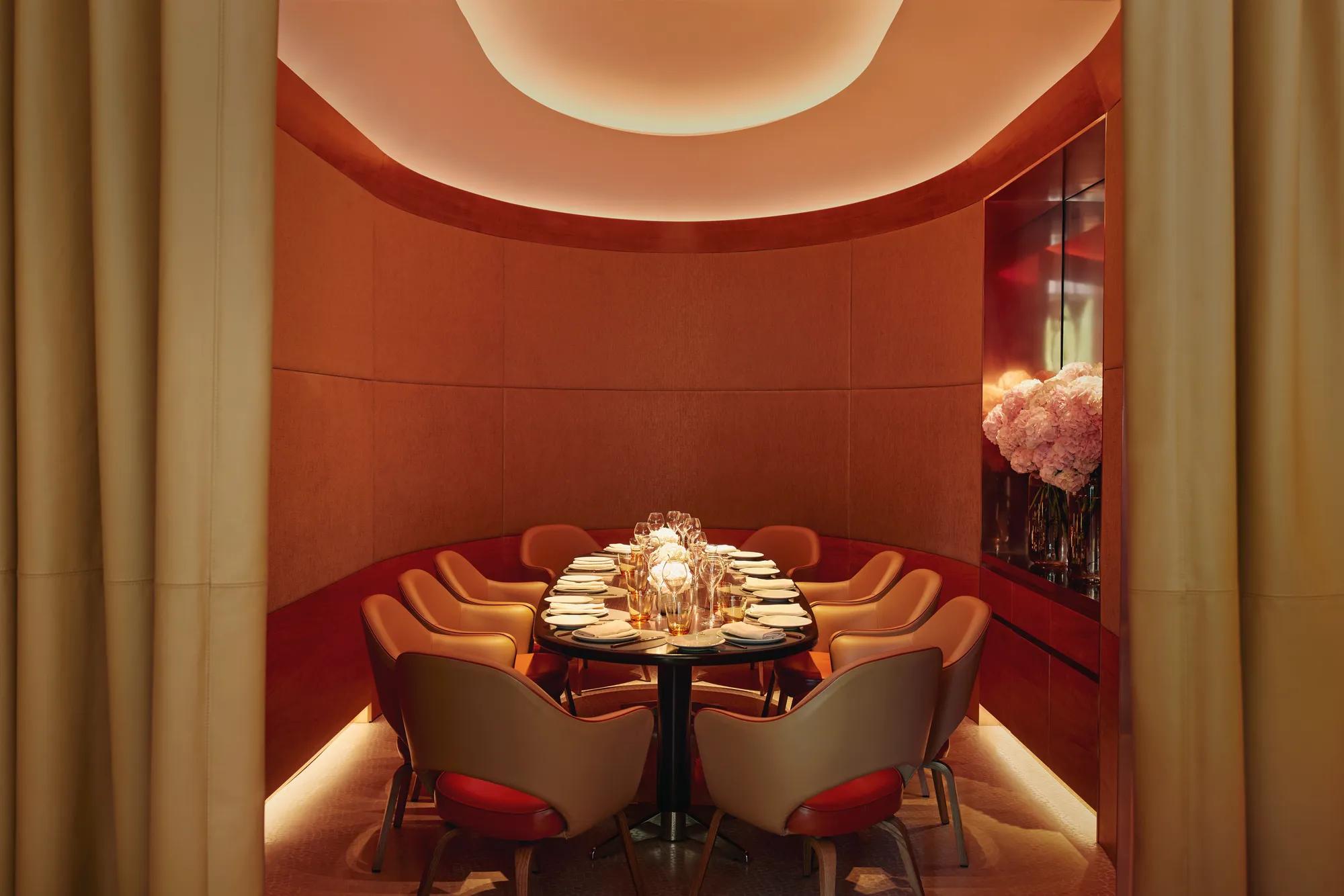 Curved private dining room with orange chairs, floral centerpiece, and soft ambient lighting.