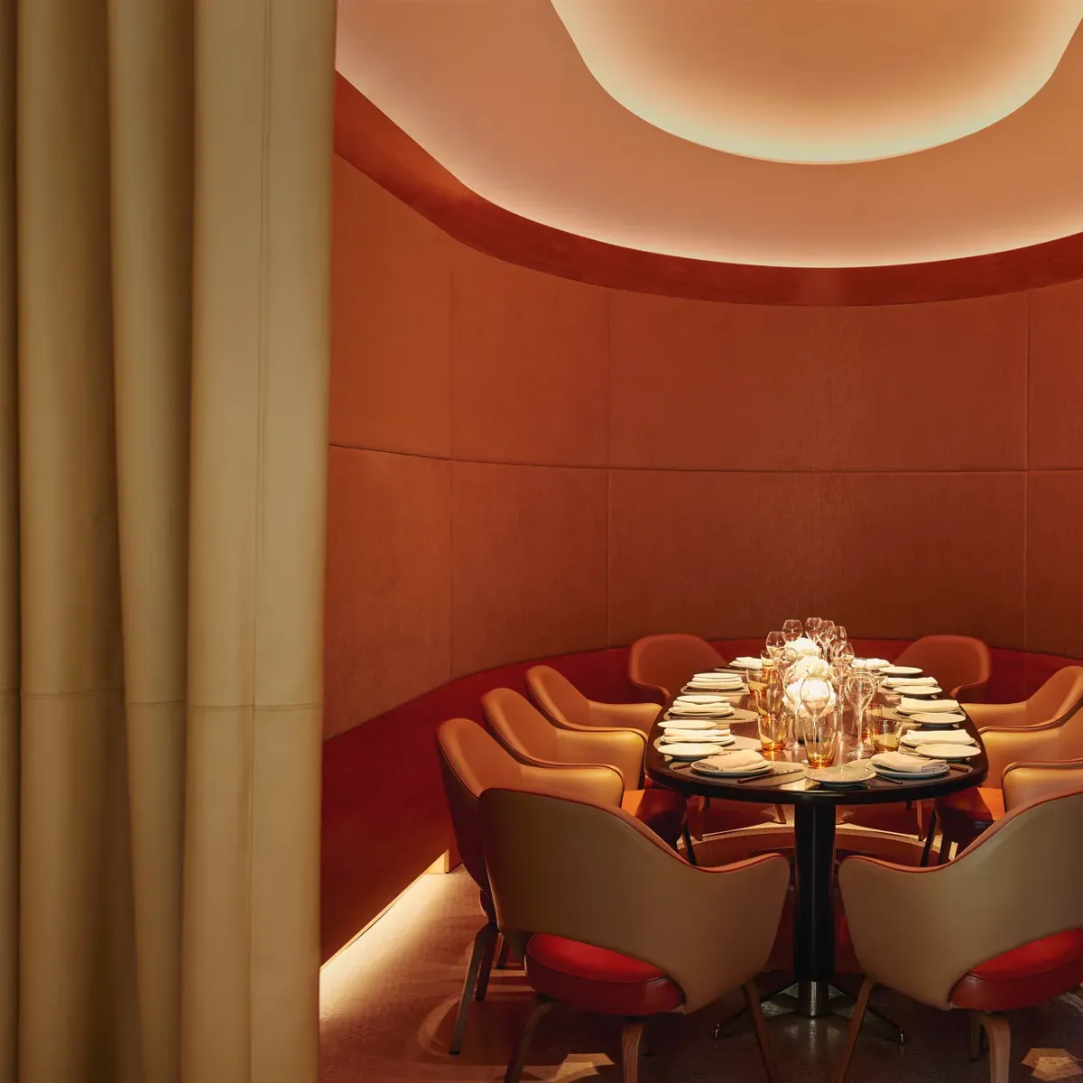 Curved private dining room with orange chairs, floral centerpiece, and soft ambient lighting.