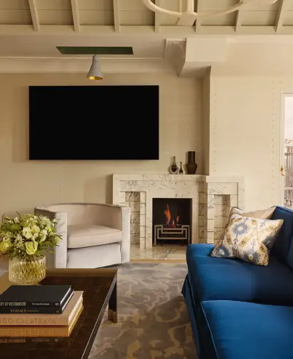 Contemporary living space with blue sofa, marble fireplace, armchair, and wall-mounted TV.