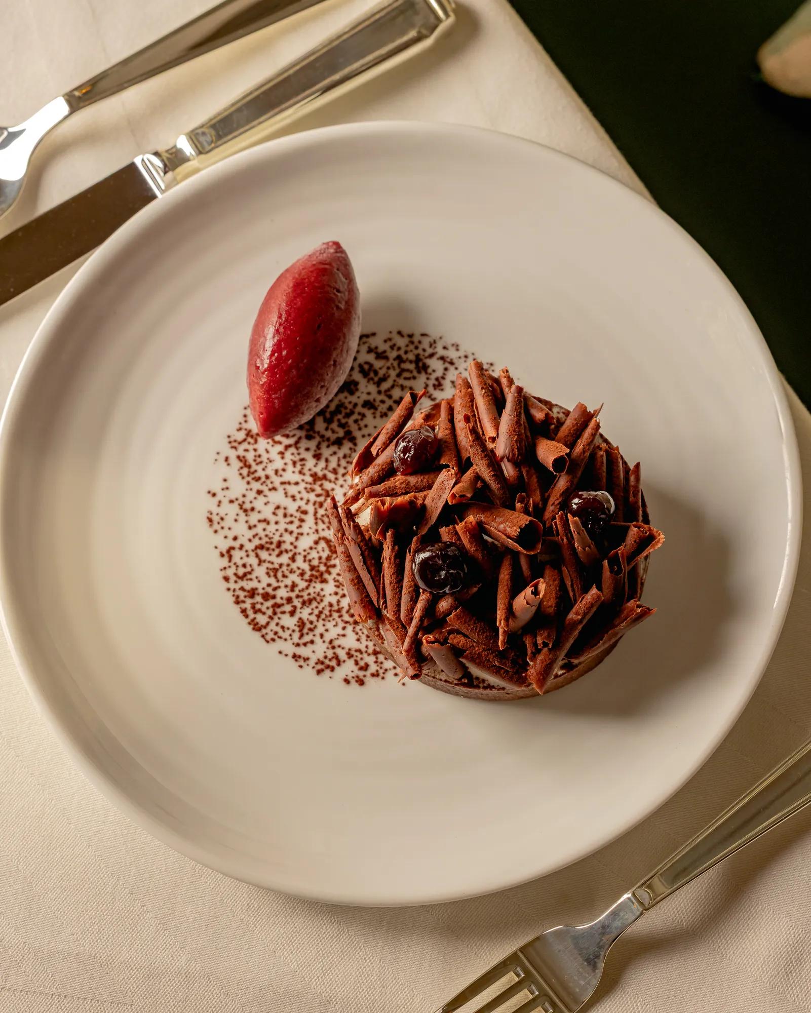 A chocolate dessert with berry sorbet served on a white plate.