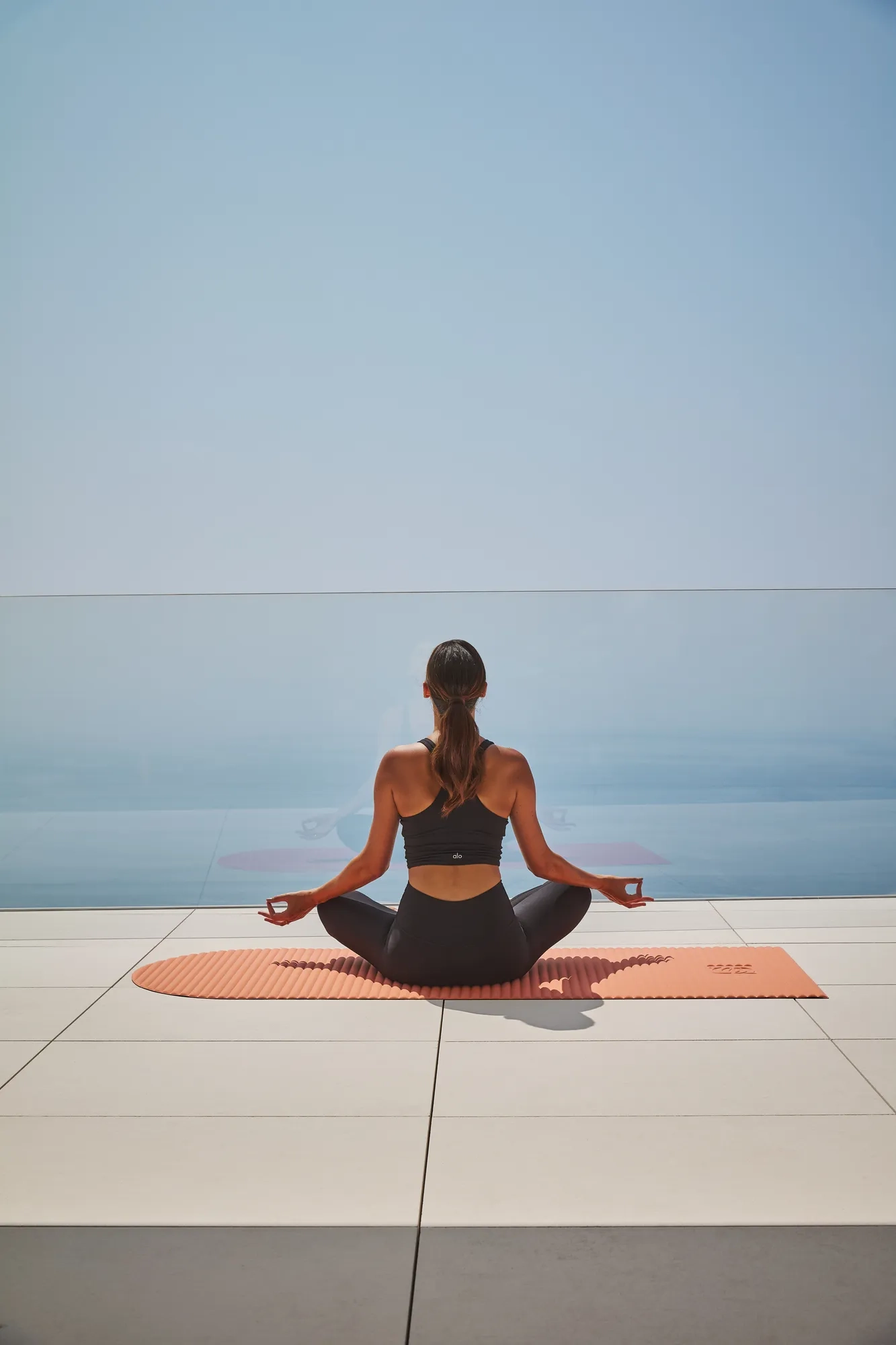Guest meditating on a yoga mat overlooking the sea, seated in a calm, open-air setting.