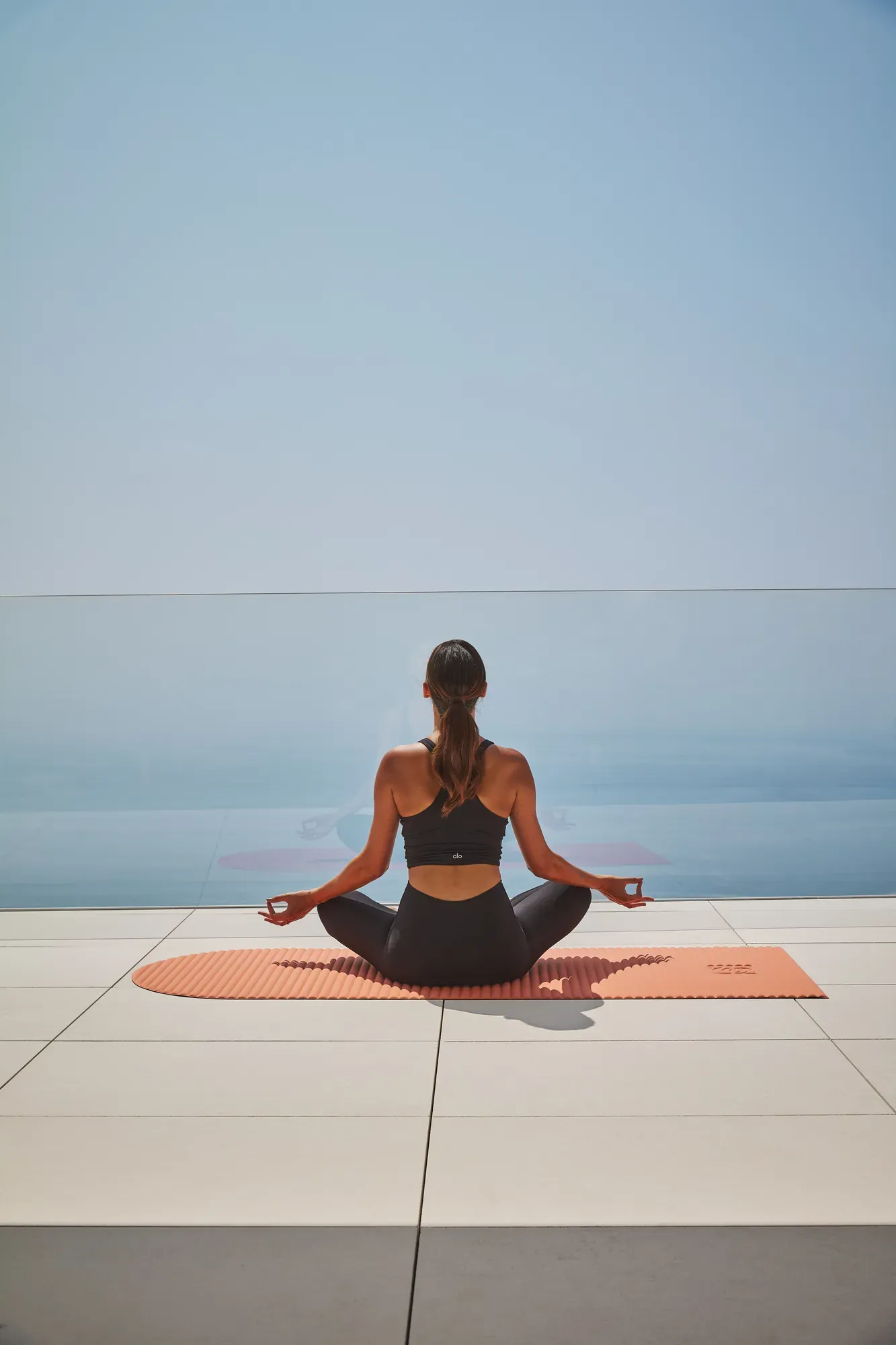 Guest meditating on a yoga mat overlooking the sea, seated in a calm, open-air setting.