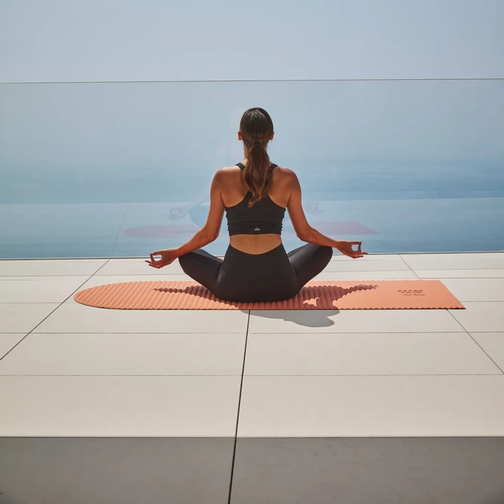 Guest meditating on a yoga mat overlooking the sea, seated in a calm, open-air setting.