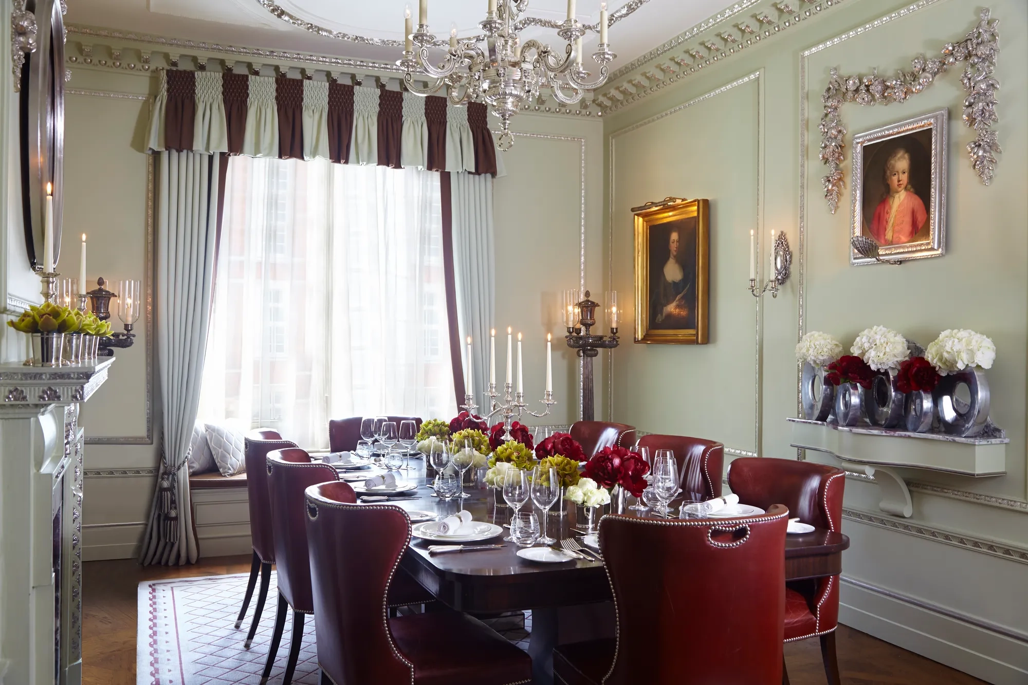 Elegant private dining room with a dark wood table, red leather chairs, floral centrepieces and classic portraits, lit by a chandelier.