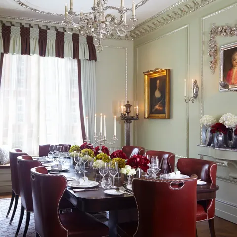 Elegant private dining room with a dark wood table, red leather chairs, floral centrepieces and classic portraits, lit by a chandelier.
