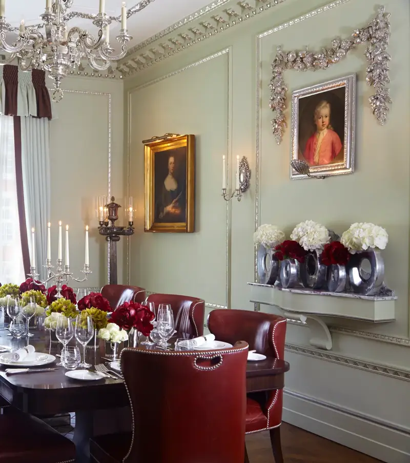 Elegant private dining room with a dark wood table, red leather chairs, floral centrepieces and classic portraits, lit by a chandelier.