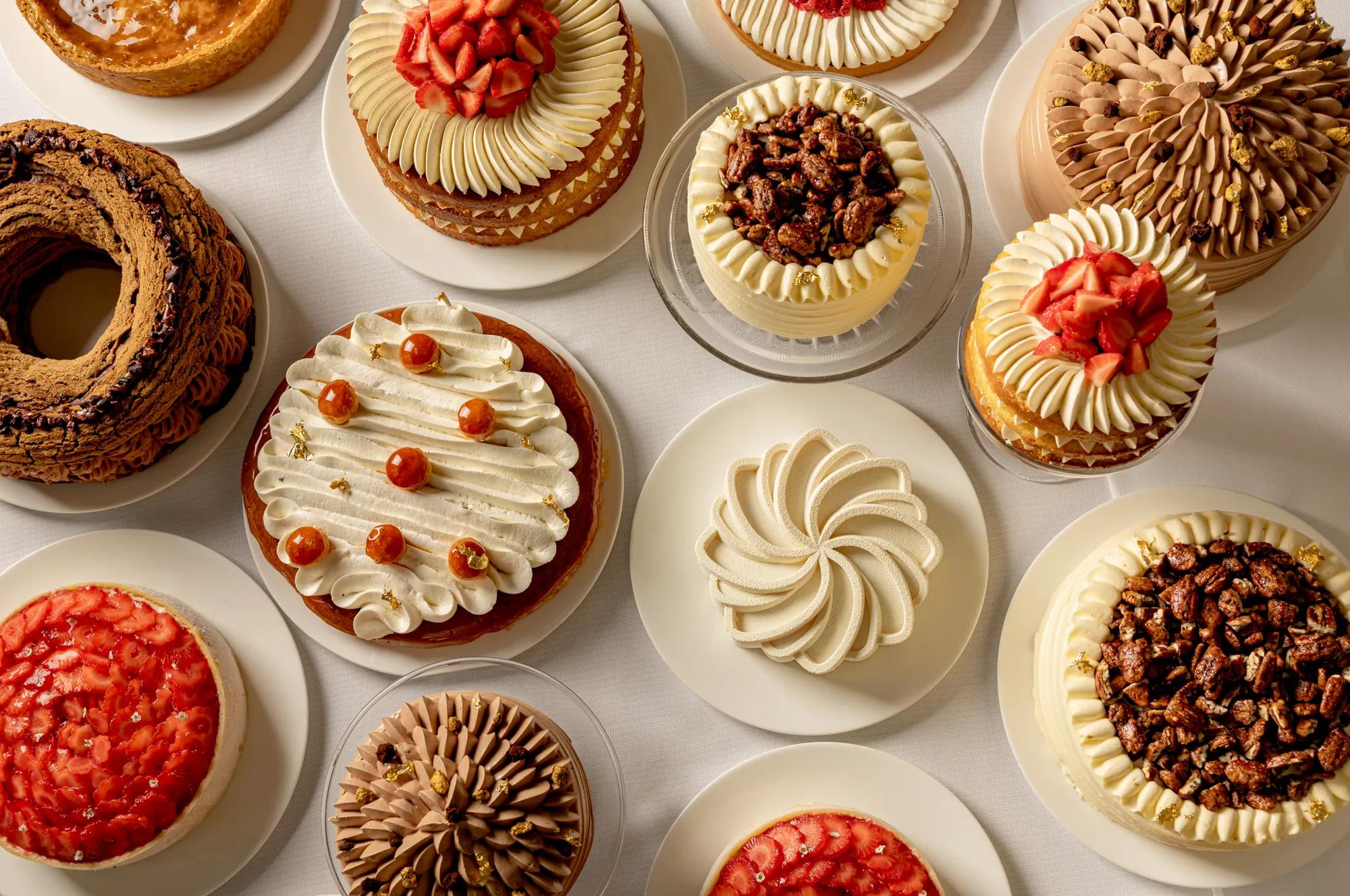 Assorted decorated cakes and tarts arranged on white plates, viewed from above.