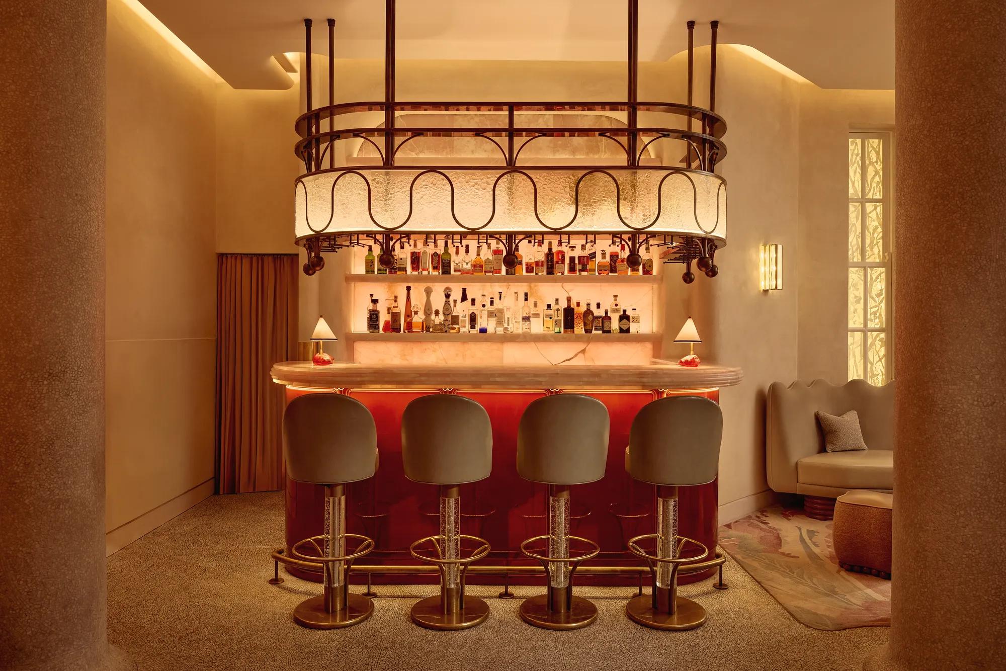 Warm, intimate bar with a glowing marble counter, curved bar stools, and a decorative overhead light feature.