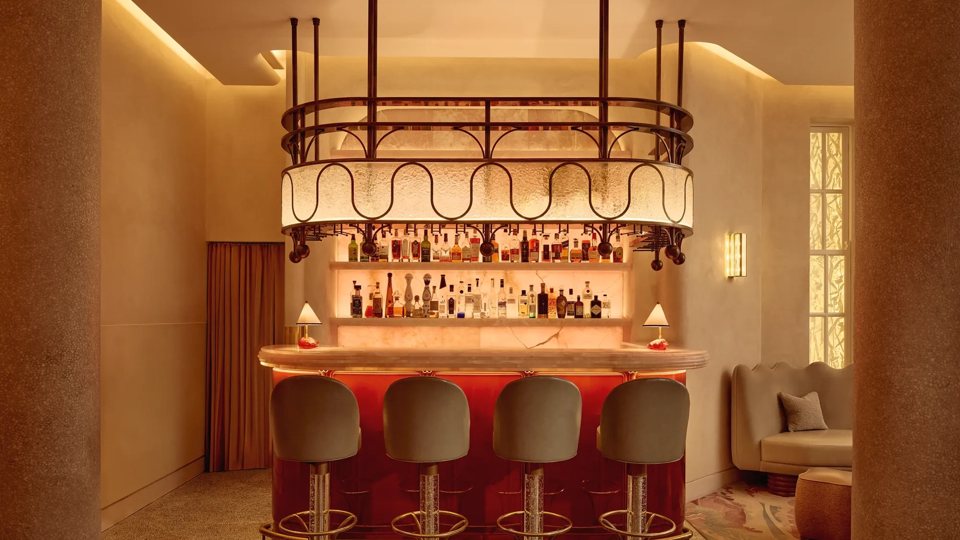 Warm, intimate bar with a glowing marble counter, curved bar stools, and a decorative overhead light feature.