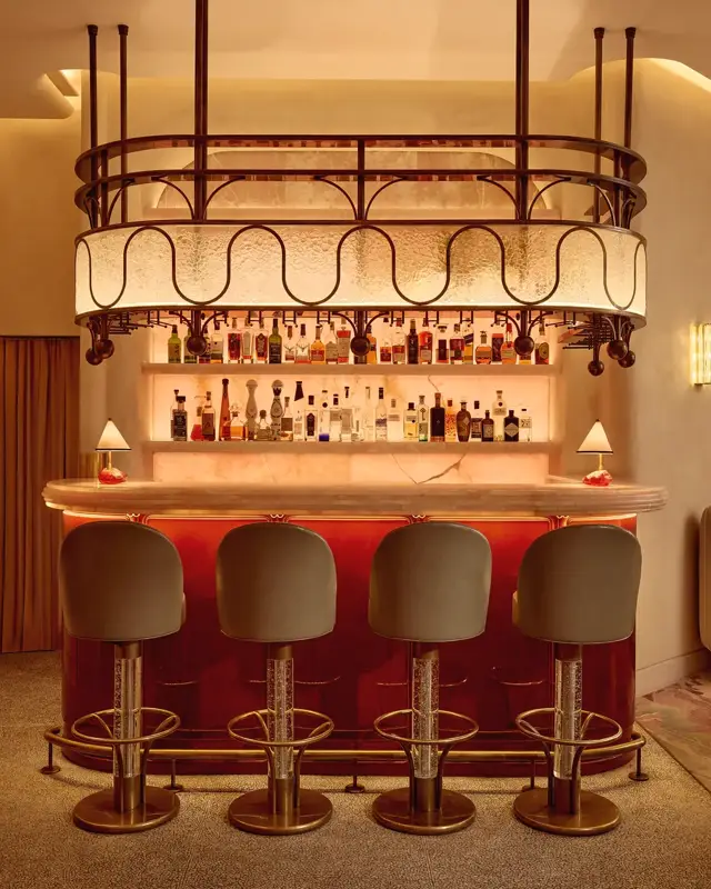 Warm, intimate bar with a glowing marble counter, curved bar stools, and a decorative overhead light feature.