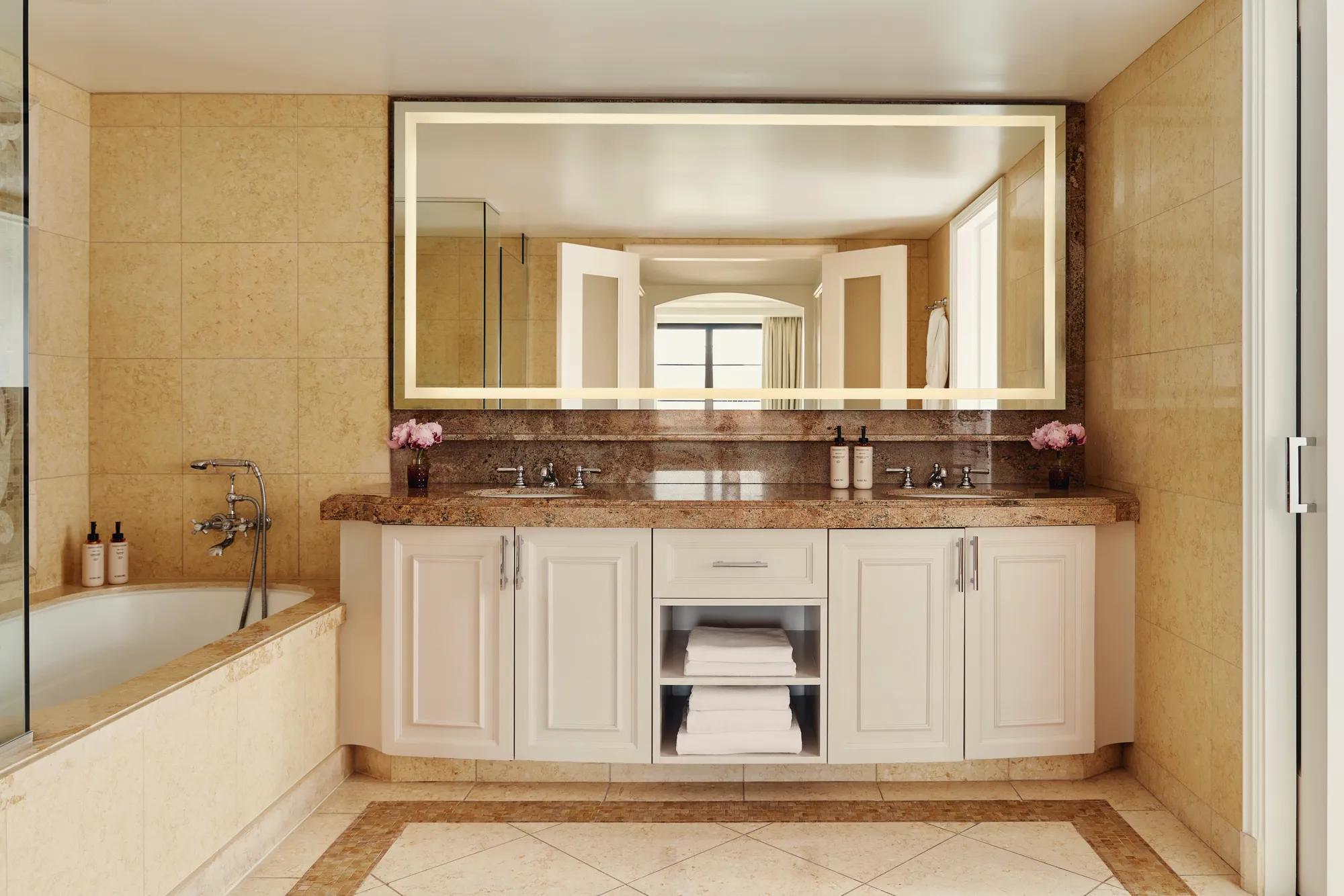 Spacious bathroom with granite double vanity, large backlit mirror, and a soaking tub with handheld shower.