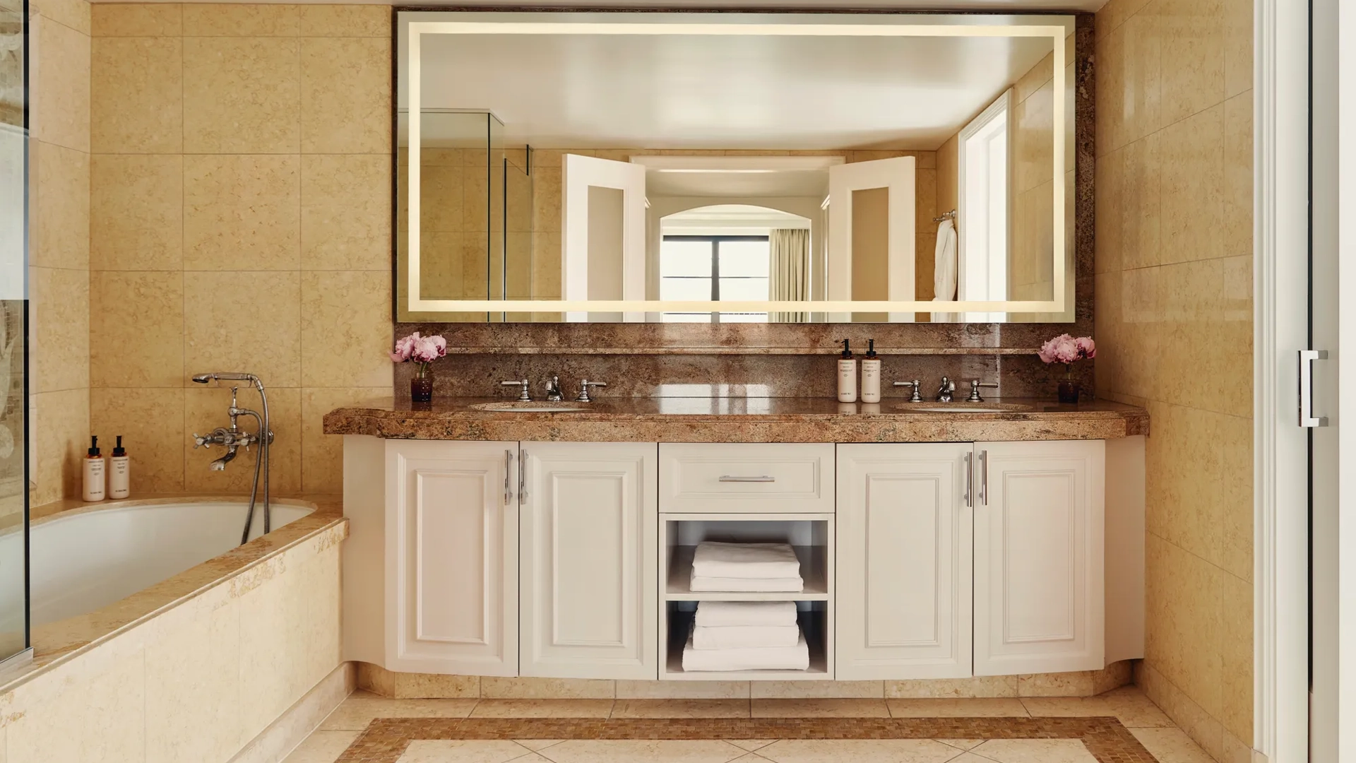 Spacious bathroom with granite double vanity, large backlit mirror, and a soaking tub with handheld shower.