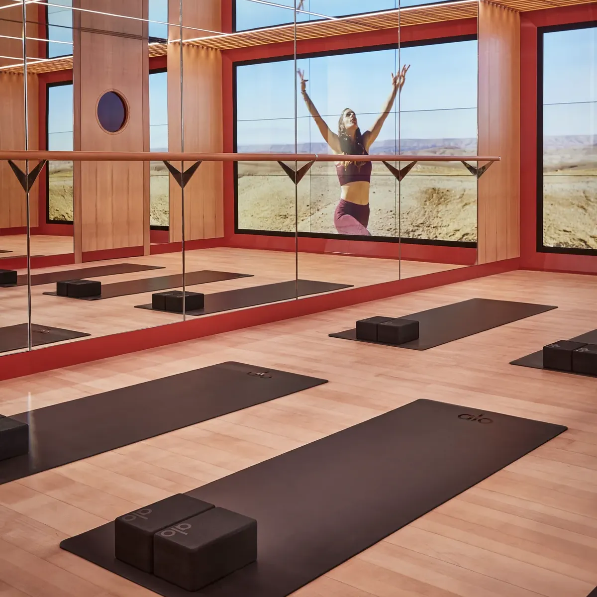 Mirrored yoga studio with mats and blocks, reflecting a woman practicing poses against expansive desert landscape.