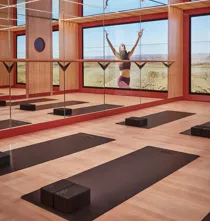 Mirrored yoga studio with mats and blocks, reflecting a woman practicing poses against expansive desert landscape.