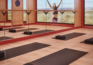Mirrored yoga studio with mats and blocks, reflecting a woman practicing poses against expansive desert landscape.