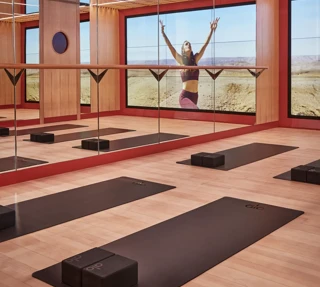 Mirrored yoga studio with mats and blocks, reflecting a woman practicing poses against expansive desert landscape.