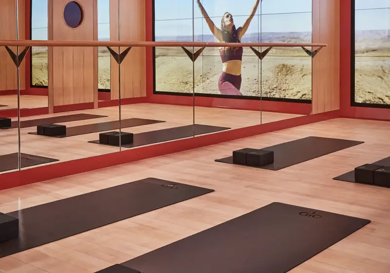 Mirrored yoga studio with mats and blocks, reflecting a woman practicing poses against expansive desert landscape.
