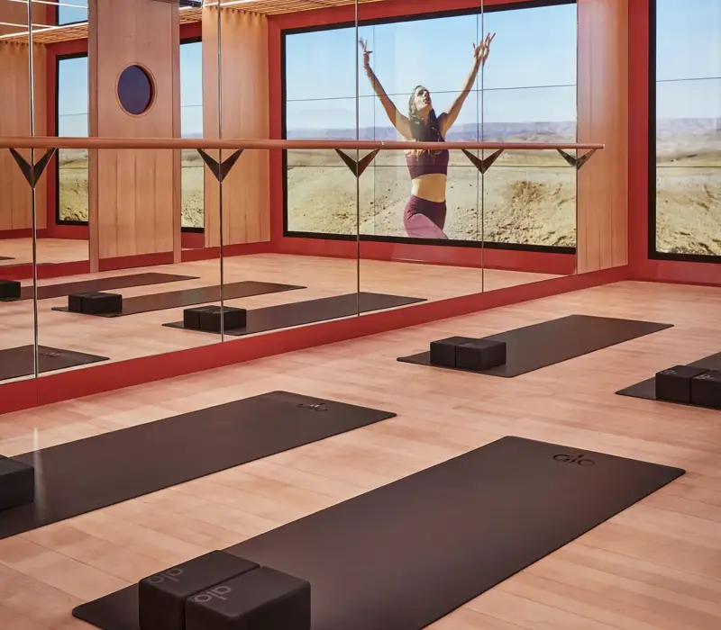 Mirrored yoga studio with mats and blocks, reflecting a woman practicing poses against expansive desert landscape.