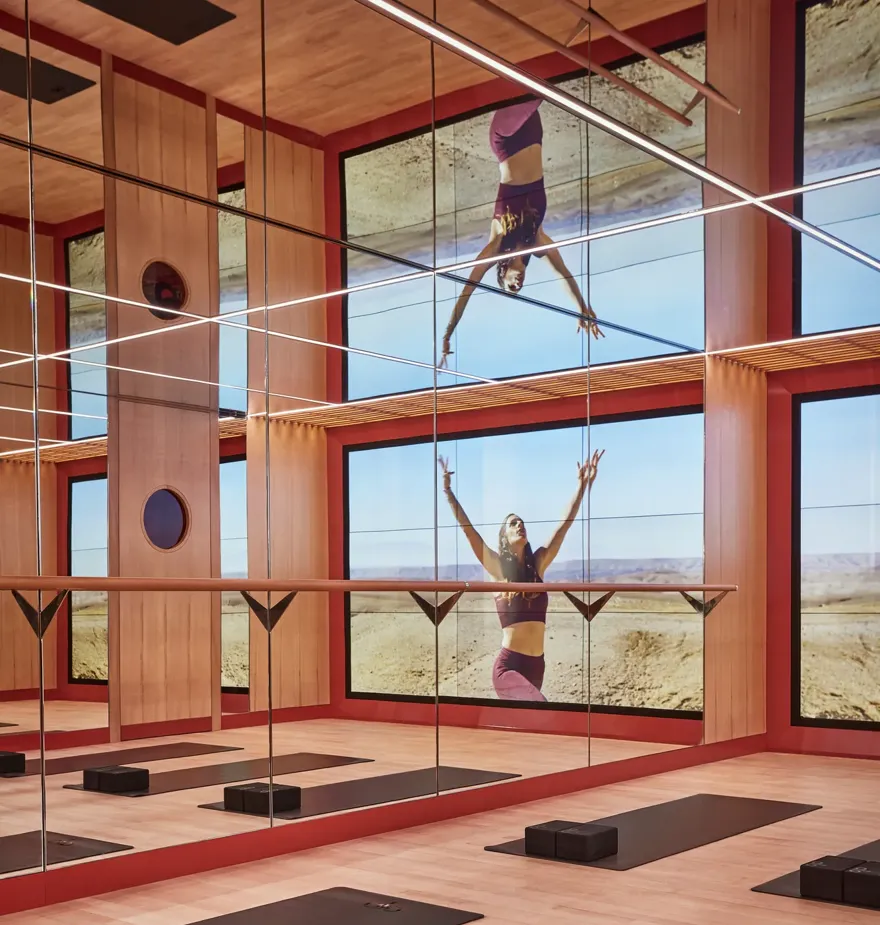 Mirrored yoga studio with mats and blocks, reflecting a woman practicing poses against expansive desert landscape.