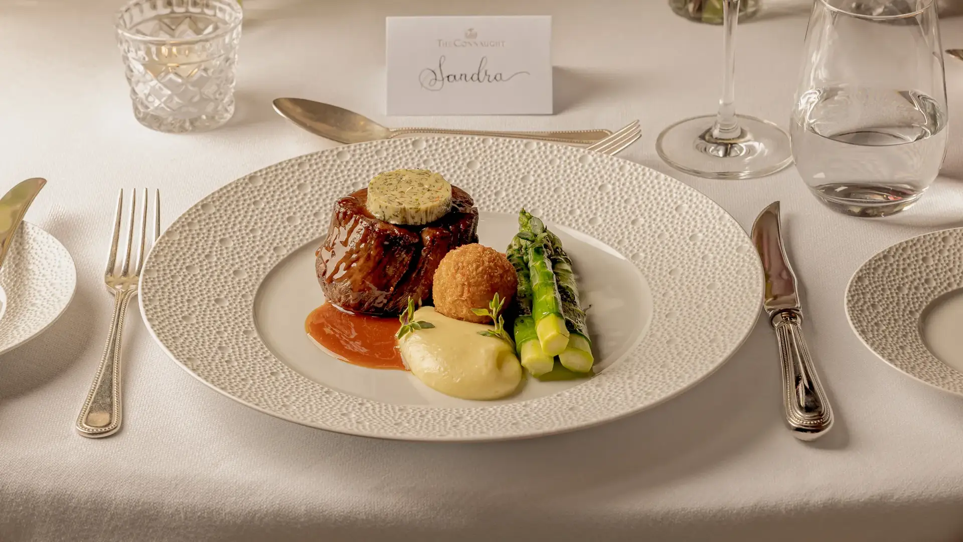 Gourmet beef dish with asparagus and potato purée served on an elegantly set dining table.