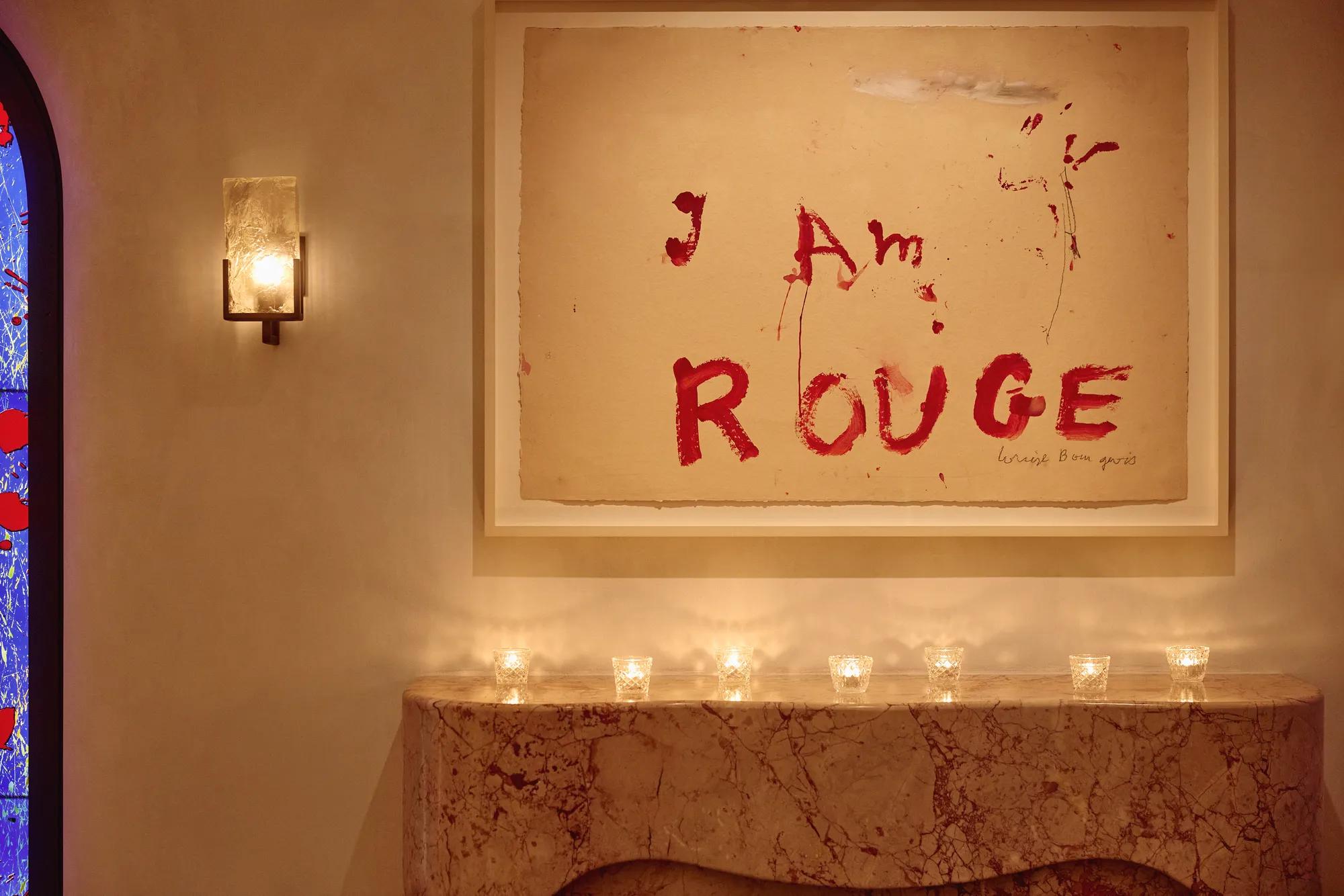 Marble mantel with small candles beneath artwork reading “I Am Rouge” in bold red text.