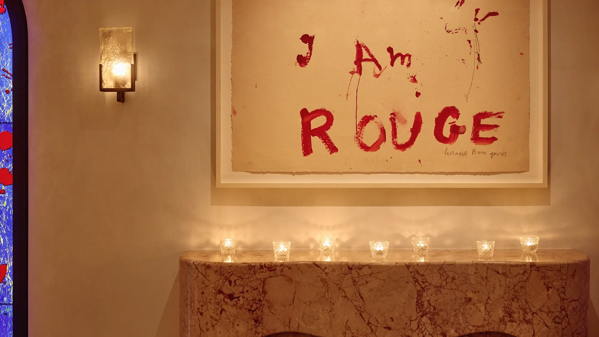 Marble mantel with small candles beneath artwork reading “I Am Rouge” in bold red text.