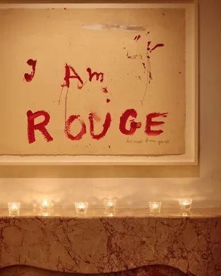 Marble mantel with small candles beneath artwork reading “I Am Rouge” in bold red text.