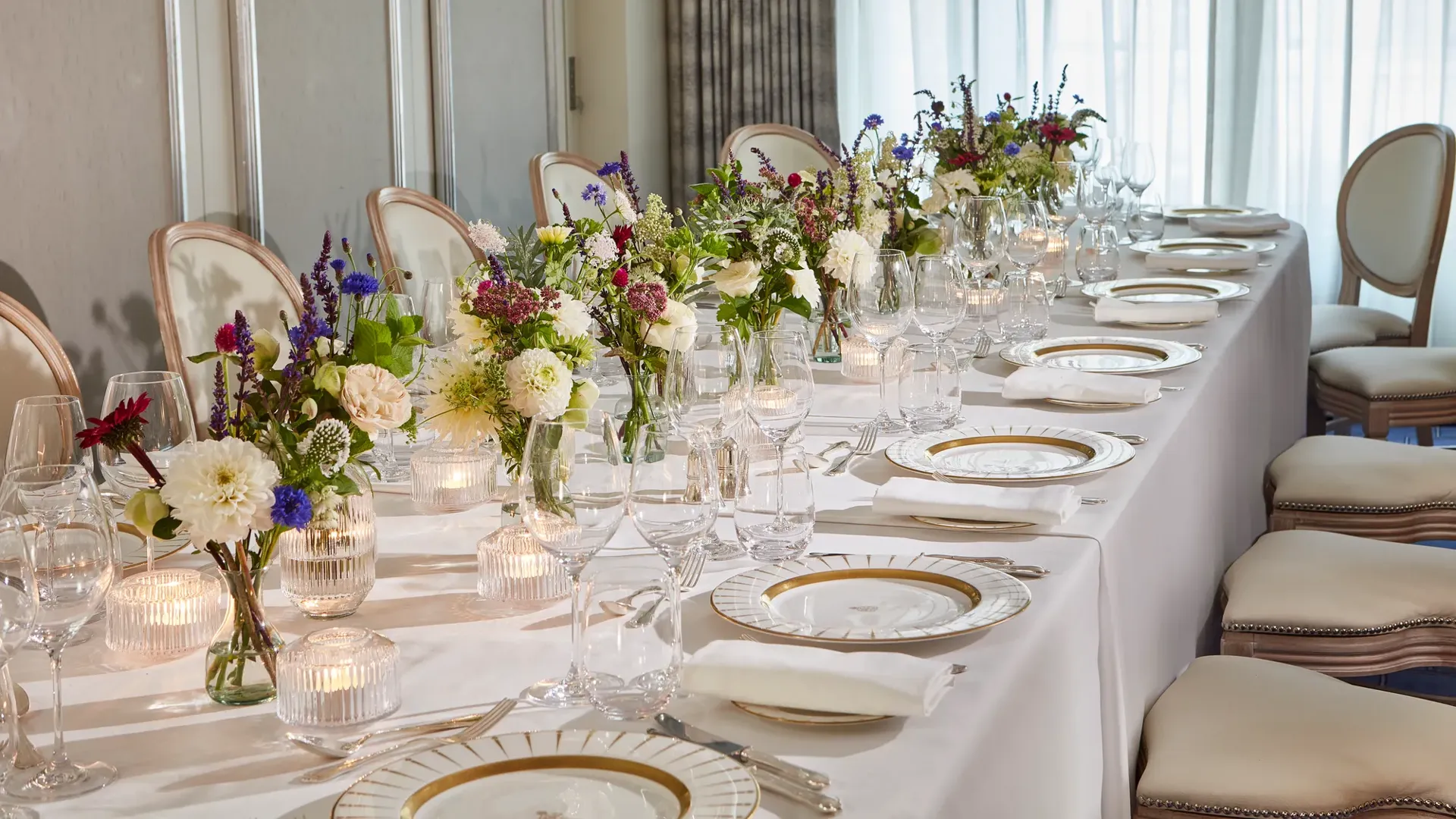 Elegant dining table at Claridge’s set with white linen, fine china, glassware, and floral centrepieces of white, purple, and pink blooms, illuminated by soft candlelight.
