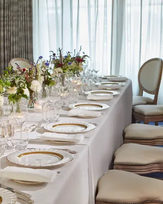 Elegant dining table at Claridge’s set with white linen, fine china, glassware, and floral centrepieces of white, purple, and pink blooms, illuminated by soft candlelight.