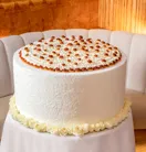 Large white frosted cake topped with piped cream and caramel drops, displayed on a table in a softly lit lounge.