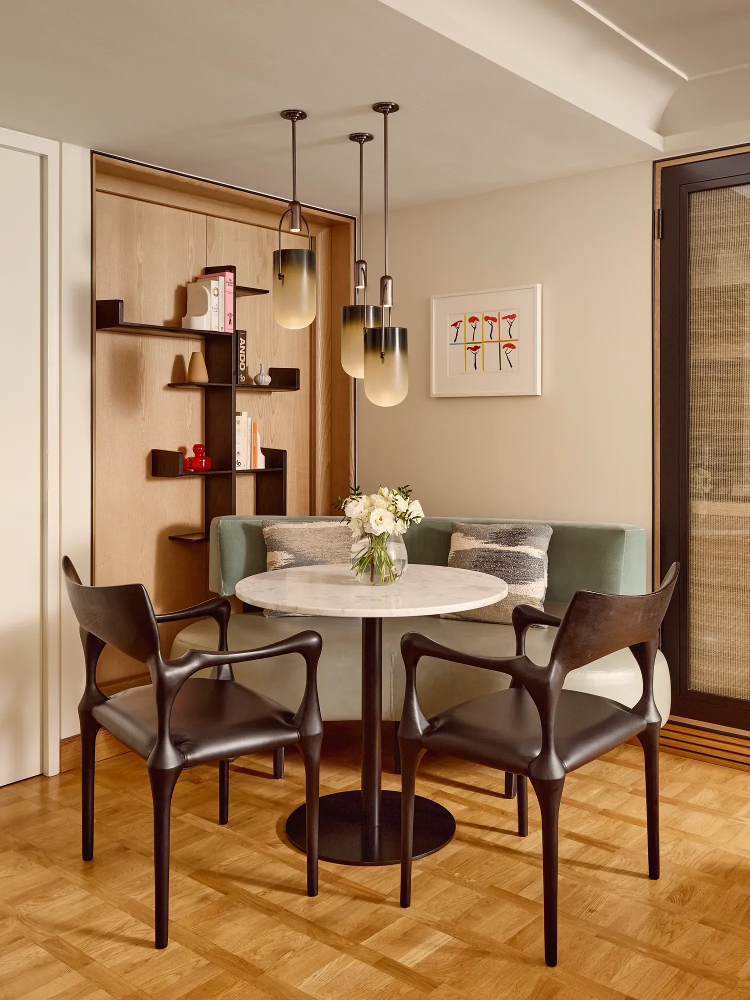 Intimate dining area with a marble-topped round table, black chairs, green banquette seating, and three amber glass pendant lights.