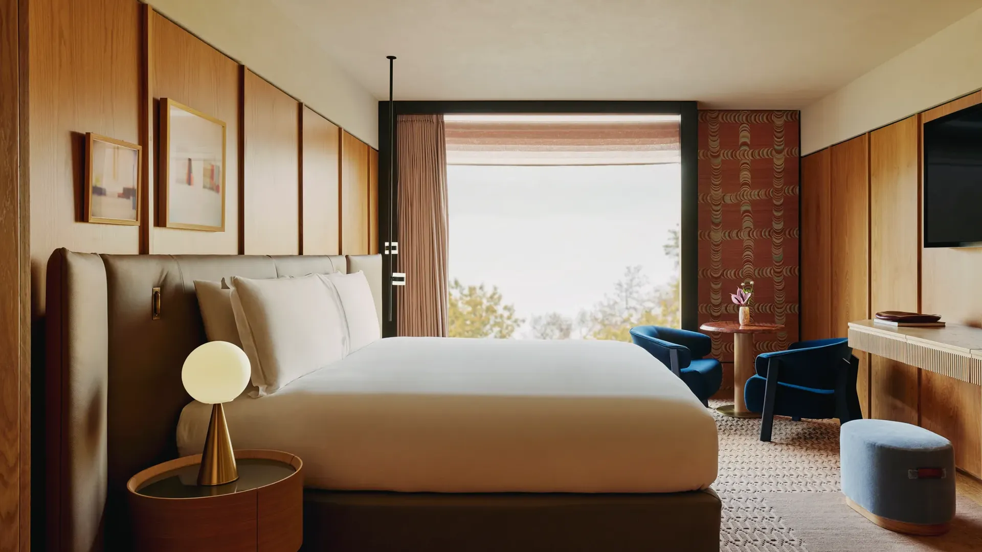Bedroom with king-size bed, warm wood panelling, seating area, and large window overlooking treetops.