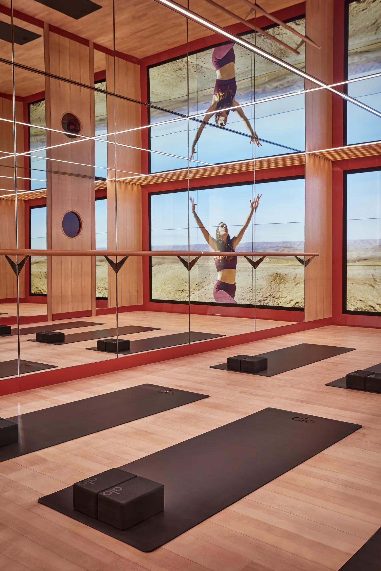 Mirrored fitness studio with yoga mats, wood floors and floor-to-ceiling screen showing wellness video.