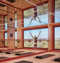 Mirrored fitness studio with yoga mats, wood floors and floor-to-ceiling screen showing wellness video.