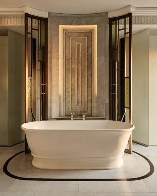 Luxurious bathroom featuring a freestanding oval bathtub set against a marble accent wall with geometric detailing and warm backlighting, framed by decorative glass and bronze panels.
