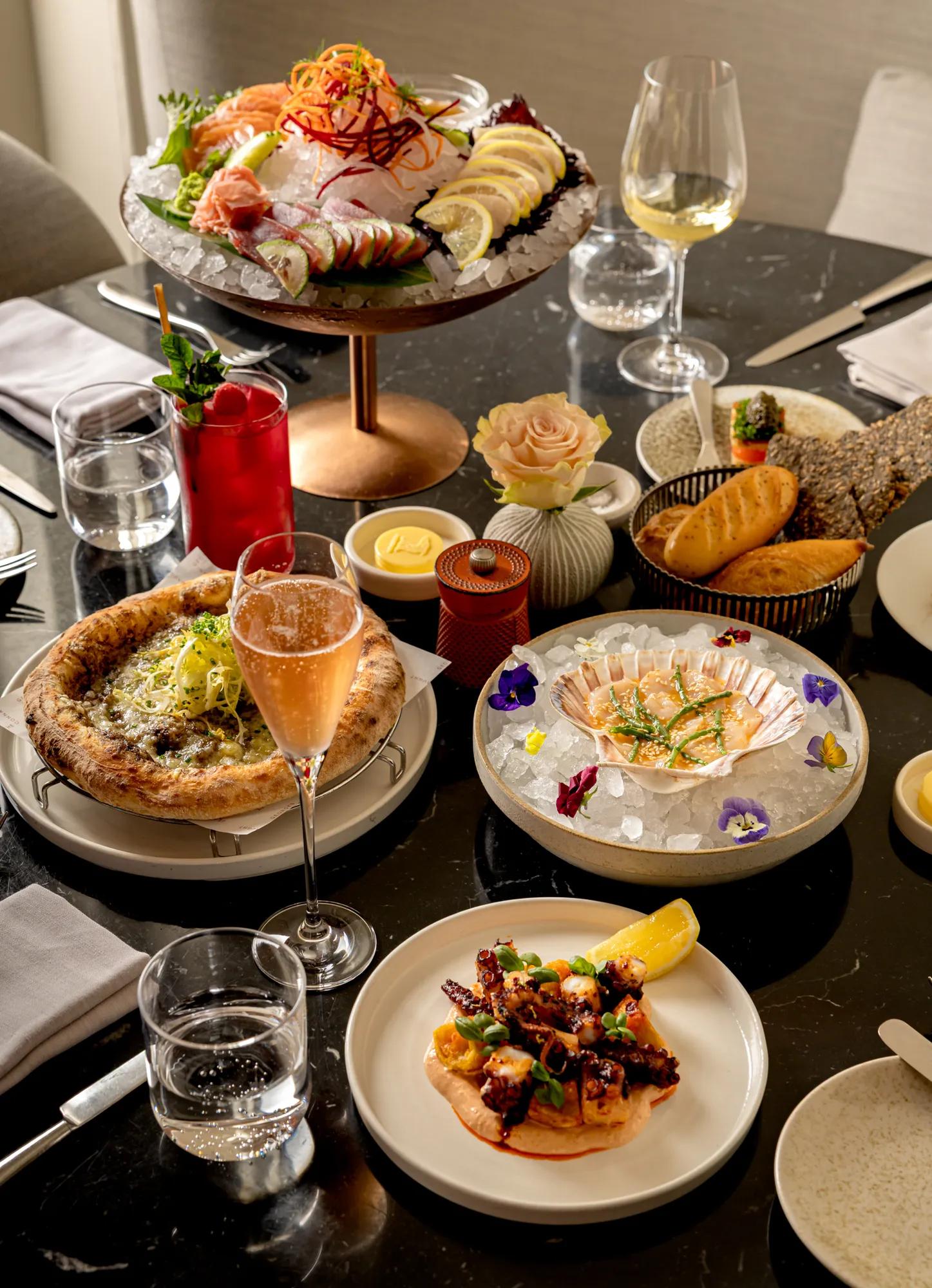 Dining table set with seafood, pizza, bread, drinks, and wine glasses.