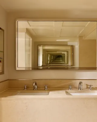 Cream marble bathroom with a double vanity and two sinks, chrome fixtures, and a large mirror creating a repeating reflection effect across the space.