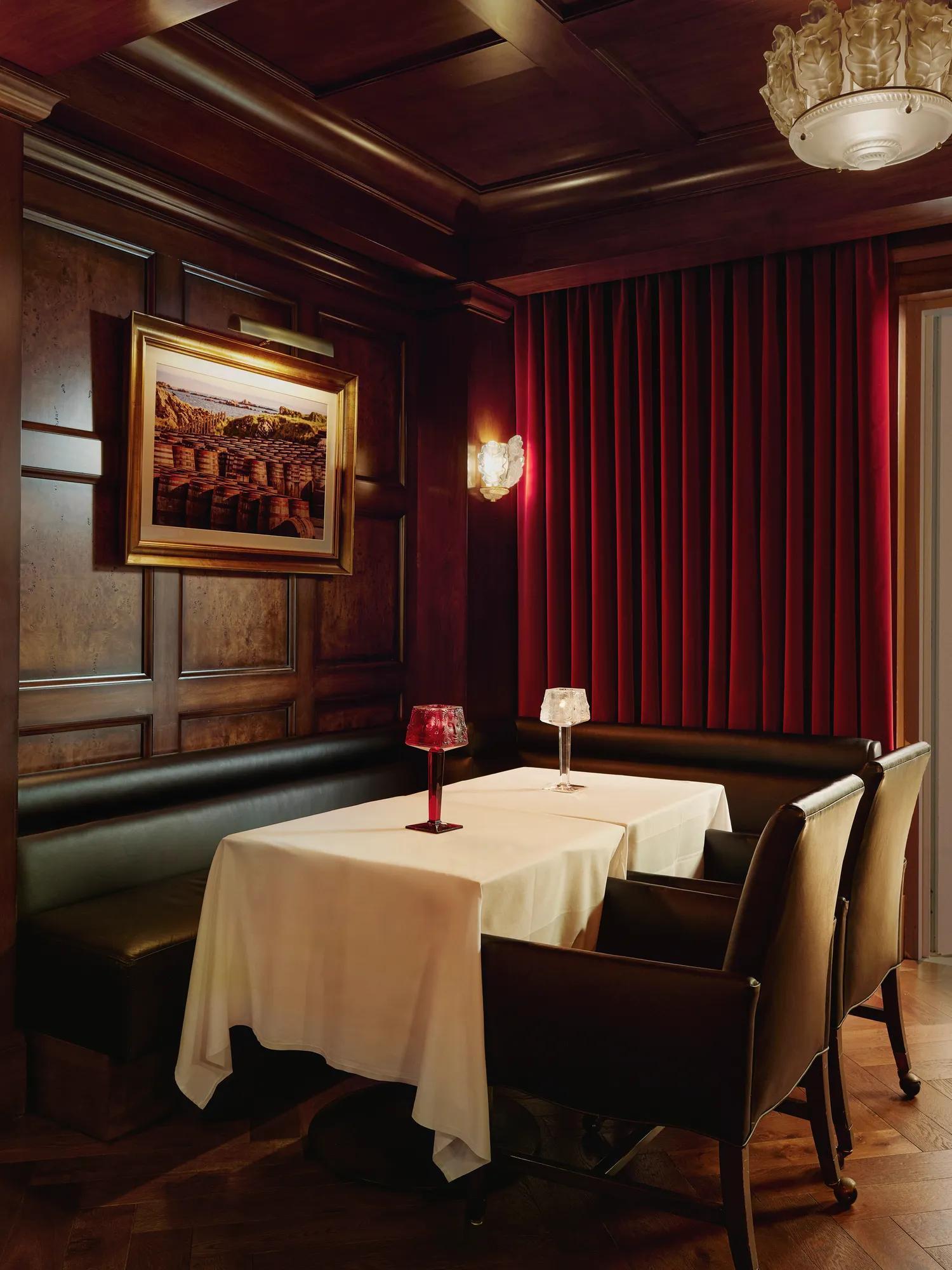 Intimate booth with white tablecloth, black leather seating, red drapes, and crystal table lamps.
