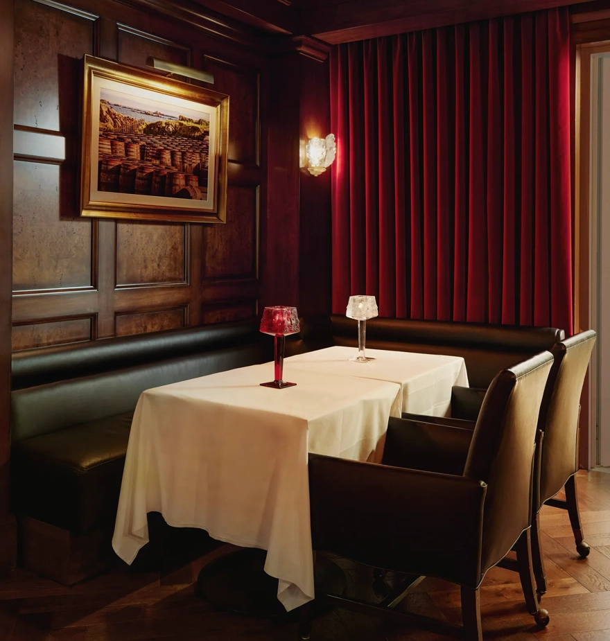 Intimate booth with white tablecloth, black leather seating, red drapes, and crystal table lamps.