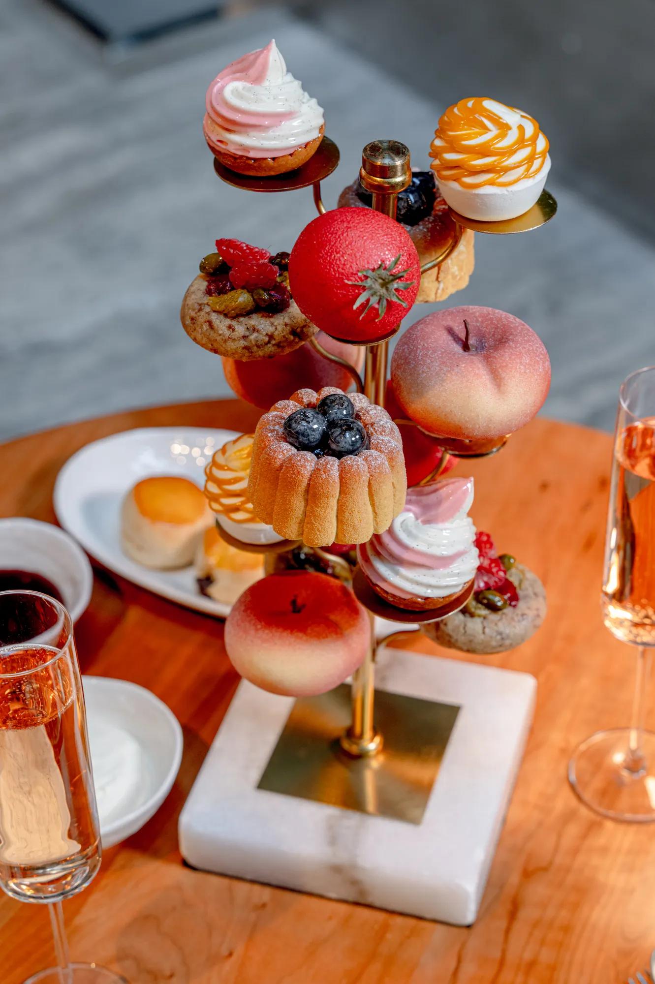 Tiered afternoon tea stand with pastries, fruit desserts and meringues arranged on gold tiers, set on a wooden table with champagne flutes.