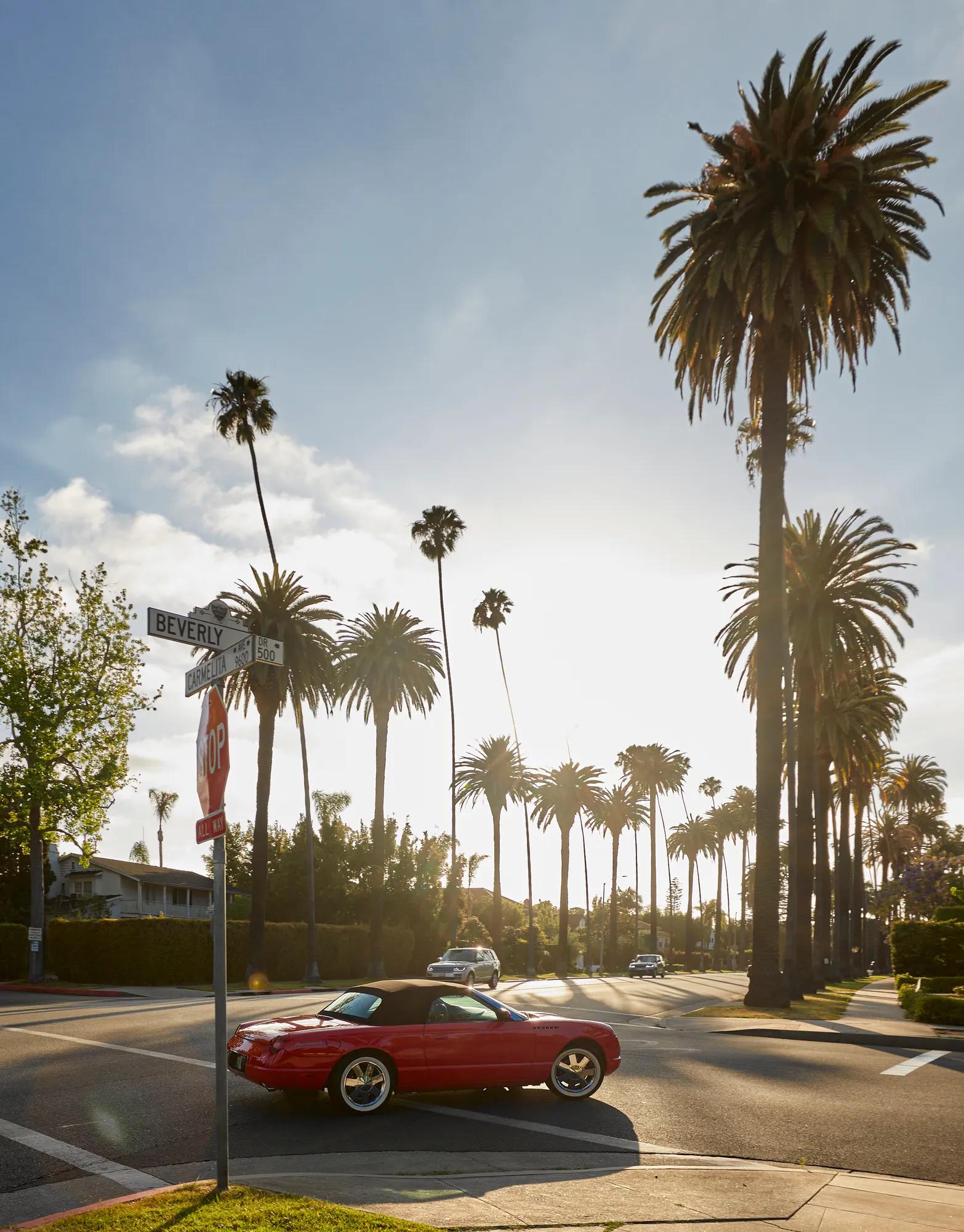 Red convertible at a palm-lined Beverly Hills intersection at golden hour.