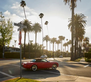 Red convertible at a palm-lined Beverly Hills intersection at golden hour.