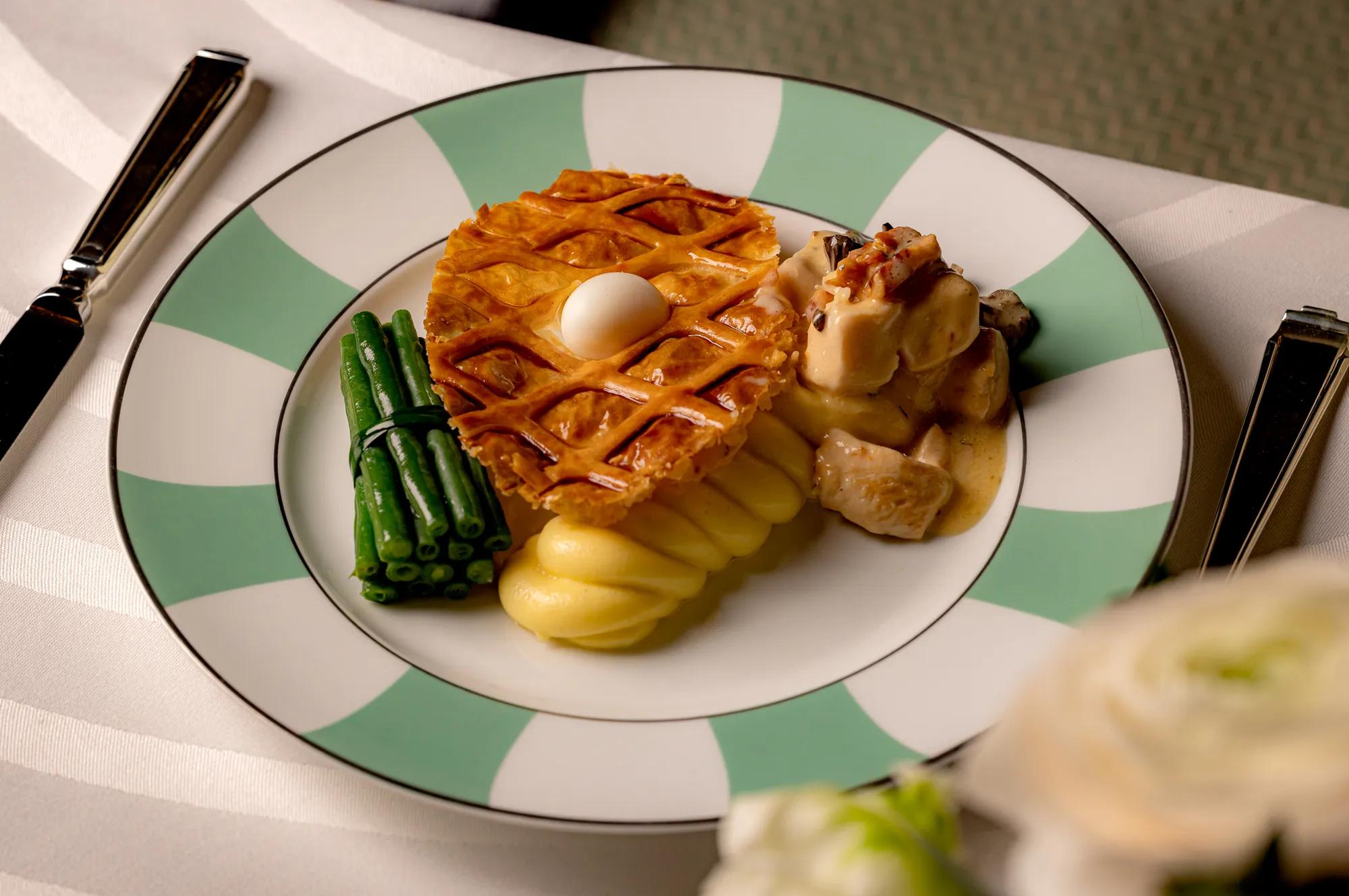 Individual serving of chicken pie with green beans, pommes Anna, and creamy chicken on a patterned plate.