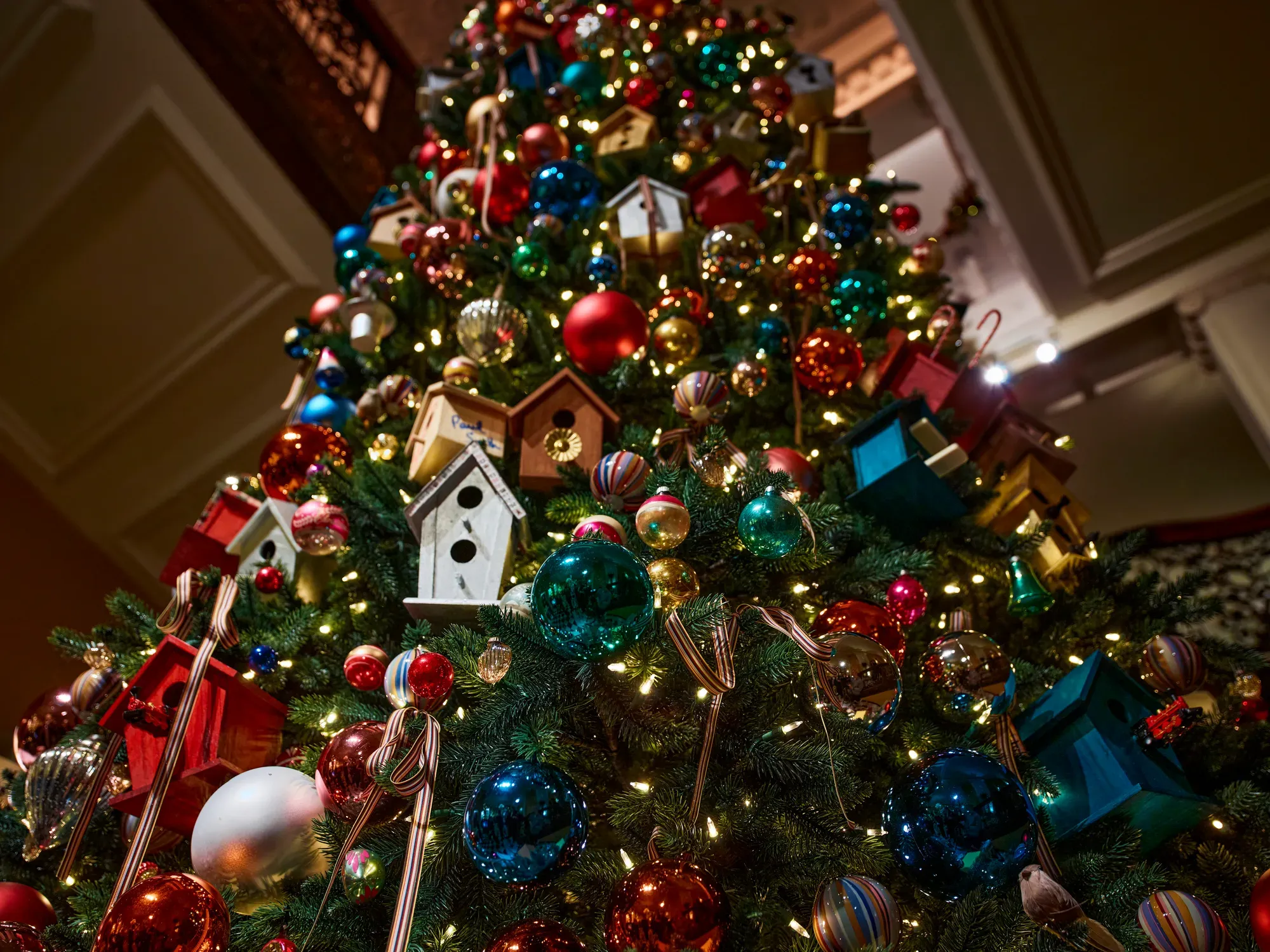 Close-up of Christmas tree with colourful baubles, birdhouse ornaments, ribbons and warm white lights